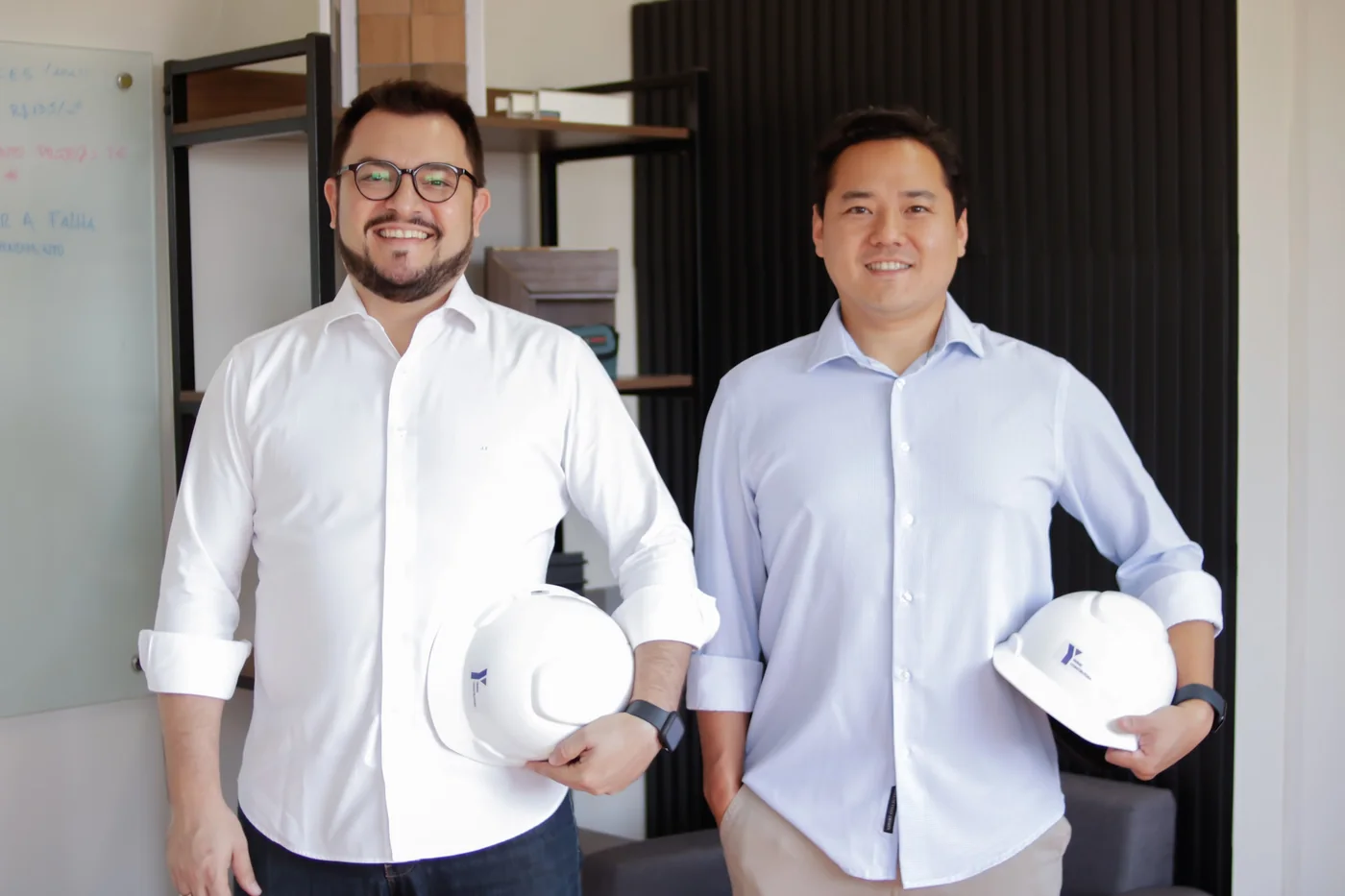 João Ferrão e Marcelo Yanai no escritório da Yanai Construtora, segurando os capacetes da empresa